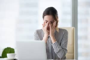Tired businesswoman massaging her eyes due to strain and fatigue, experiencing headache and eyestrain after computer work, possibly linked to overwork and hormone imbalance.