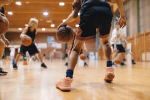 Junior-level basketball player bouncing a basketball during a training session, representing youth sports, school physical education, and preparation for a sports physical exam