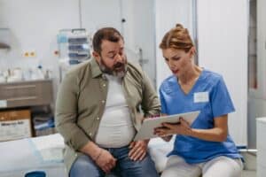 Female doctor consulting with an overweight patient in a medical office, discussing test results and the health risks of obesity, focusing on medical weight loss and its impact on middle-aged men's health.