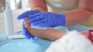 Registered nurse or pediatric surgeon treating foot wound on young girl during medical procedure for soft tissue injury care.
