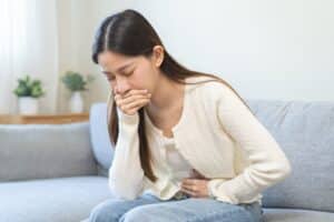 Unhappy woman holding her belly and covering her mouth, experiencing nausea and morning sickness, possibly from food poisoning