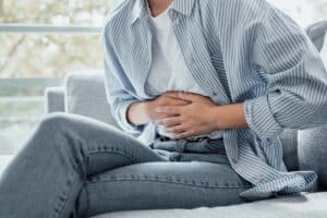 A young woman holds her stomach in pain, showing signs of constipation, indigestion, or abdominal discomfort related to gastritis, pancreatitis, or diarrhea.