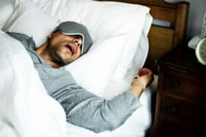 A man in a sleep mask lying on his back and snoring
