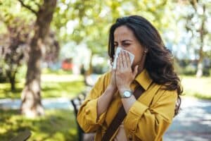 Woman sneezing outdoors experiencing common spring illnesses or seasonal allergies