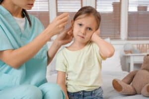 Child holding her ear during an ear infection exam at a doctor’s office.