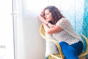Woman sitting with clasped hands and a worried expression while experiencing anxiety.