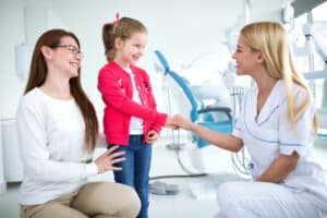 Child speaking with a primary care provider during a medical visit while her mother looks on.